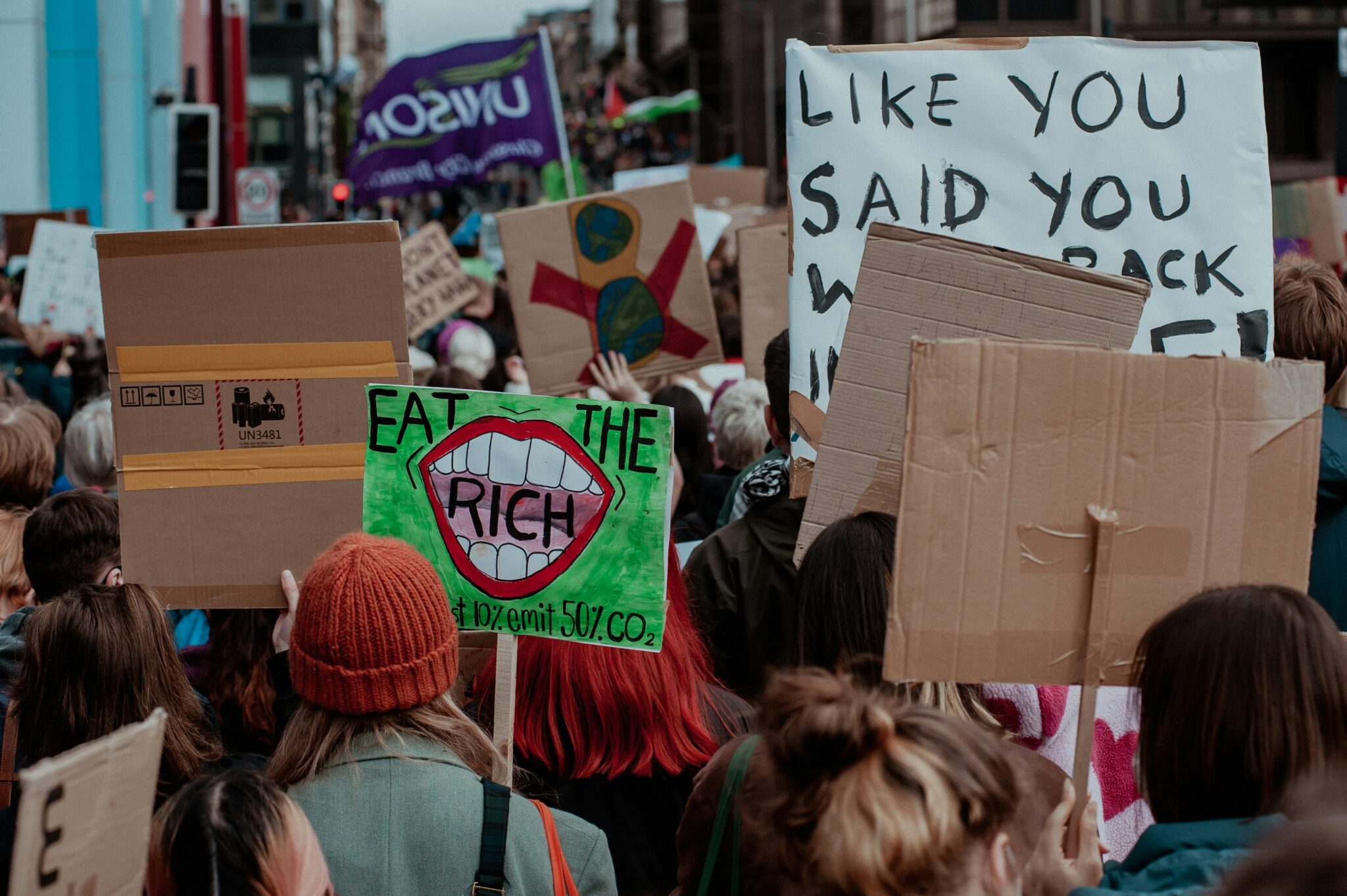 Dagtida protest. En skylt som det står "eat the rich" och "top 10% emit 50% CO2" på.
